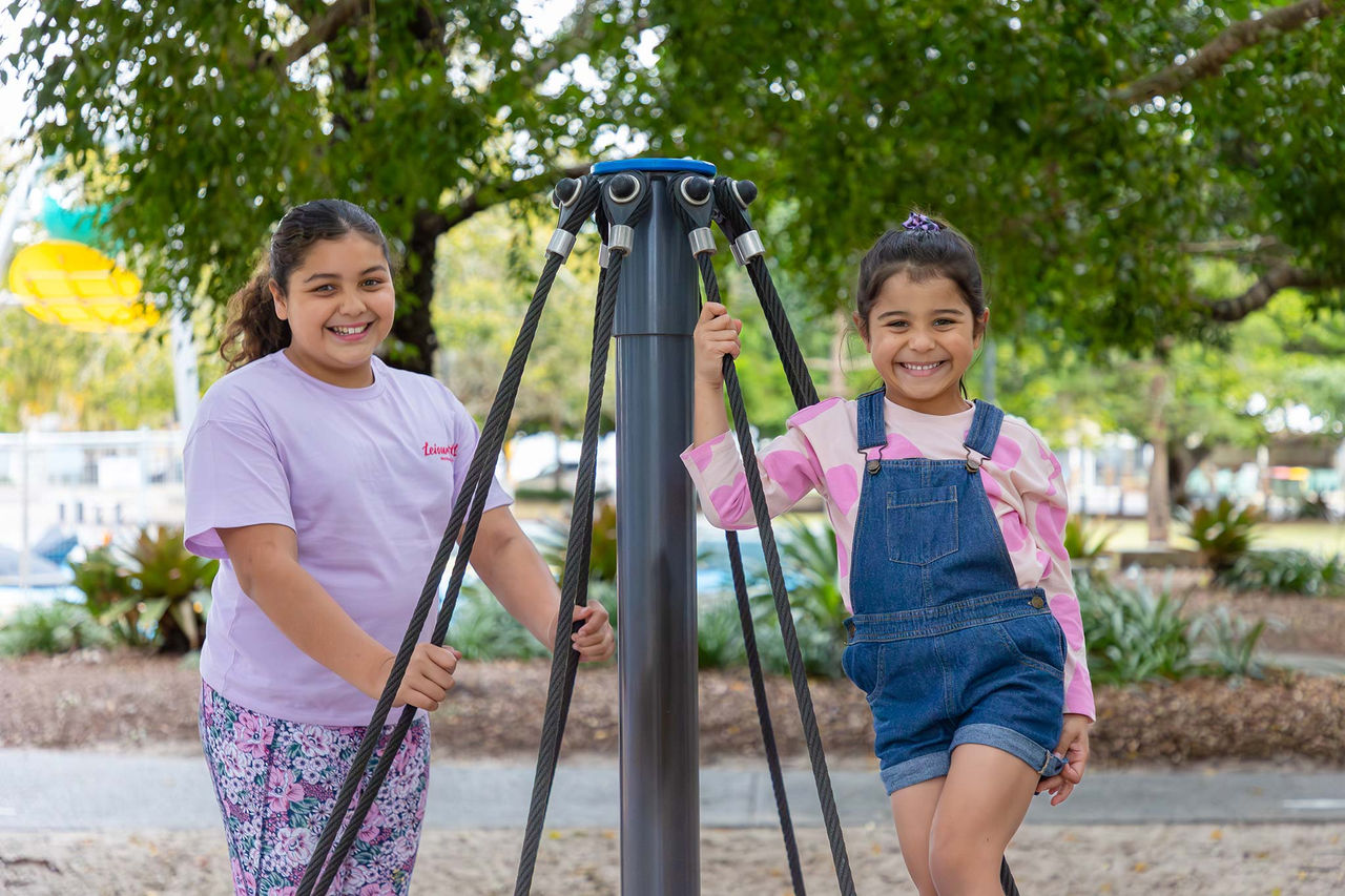 Two girls on a modern roundabout in Wynnum Wading Pool Park playground